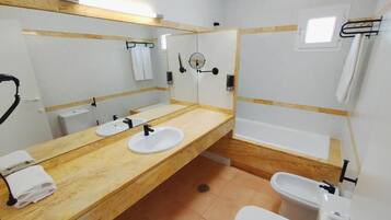 Une salle de bain avec un meuble-lavabo en bois, deux vasques, un miroir, des toilettes et une baignoire.