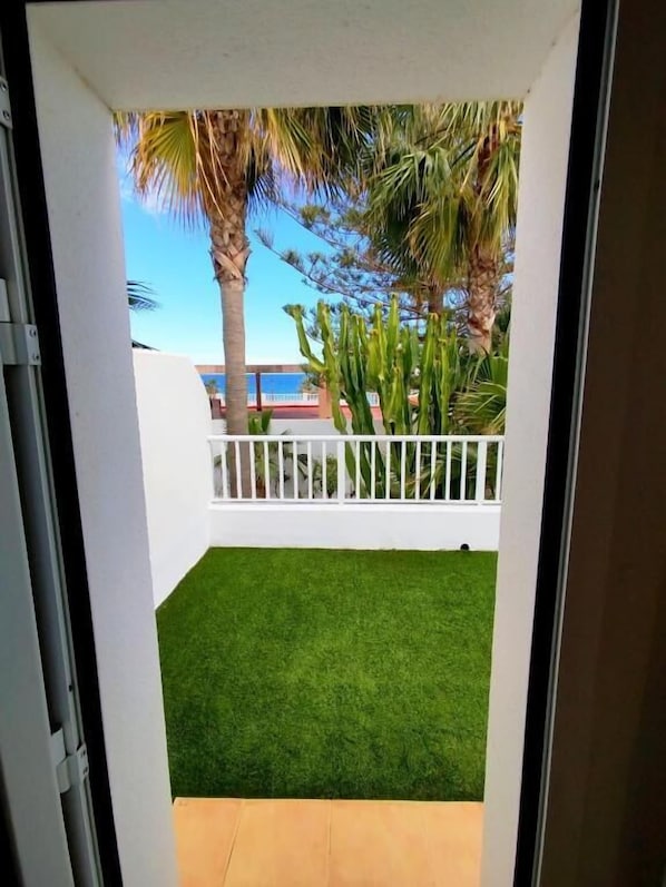 Blick durch eine Tür auf einen Balkon mit künstlichem Rasen, Palmen und einem weißen Geländer.