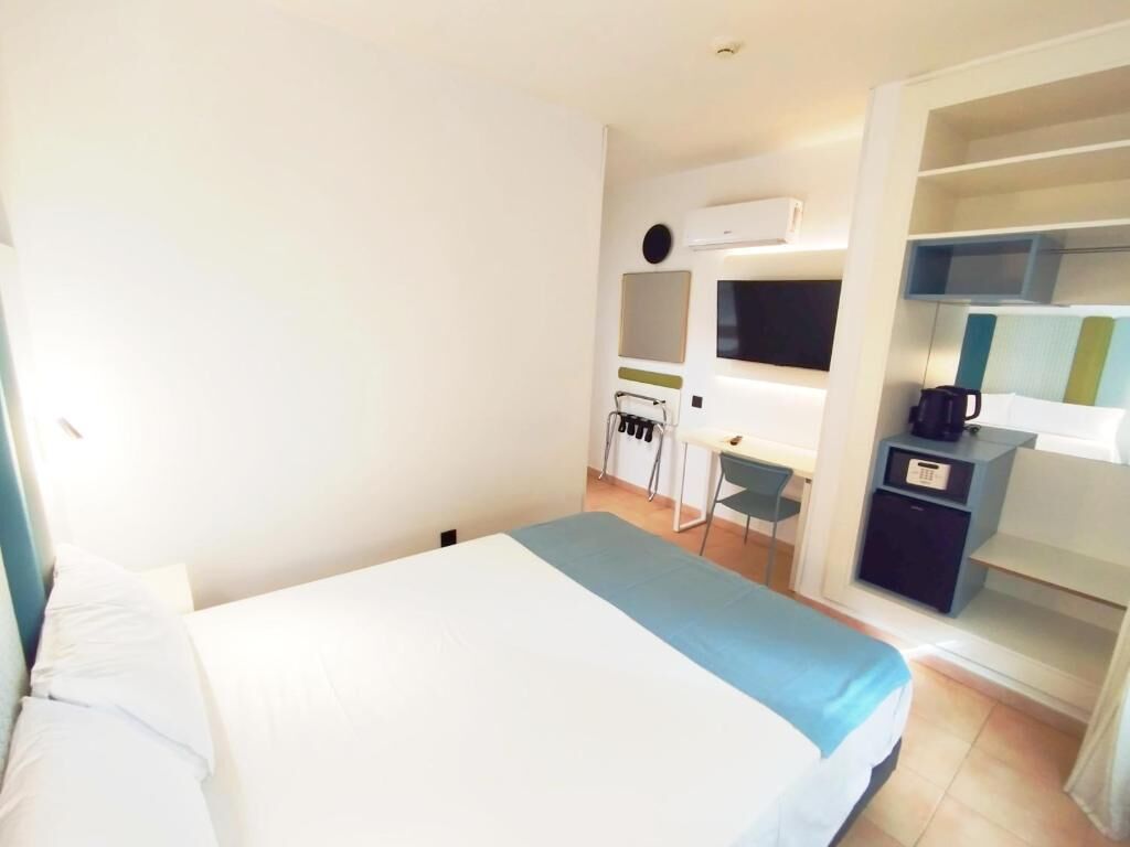 Una habitación de hotel con cama, escritorio, silla, televisor y armario.