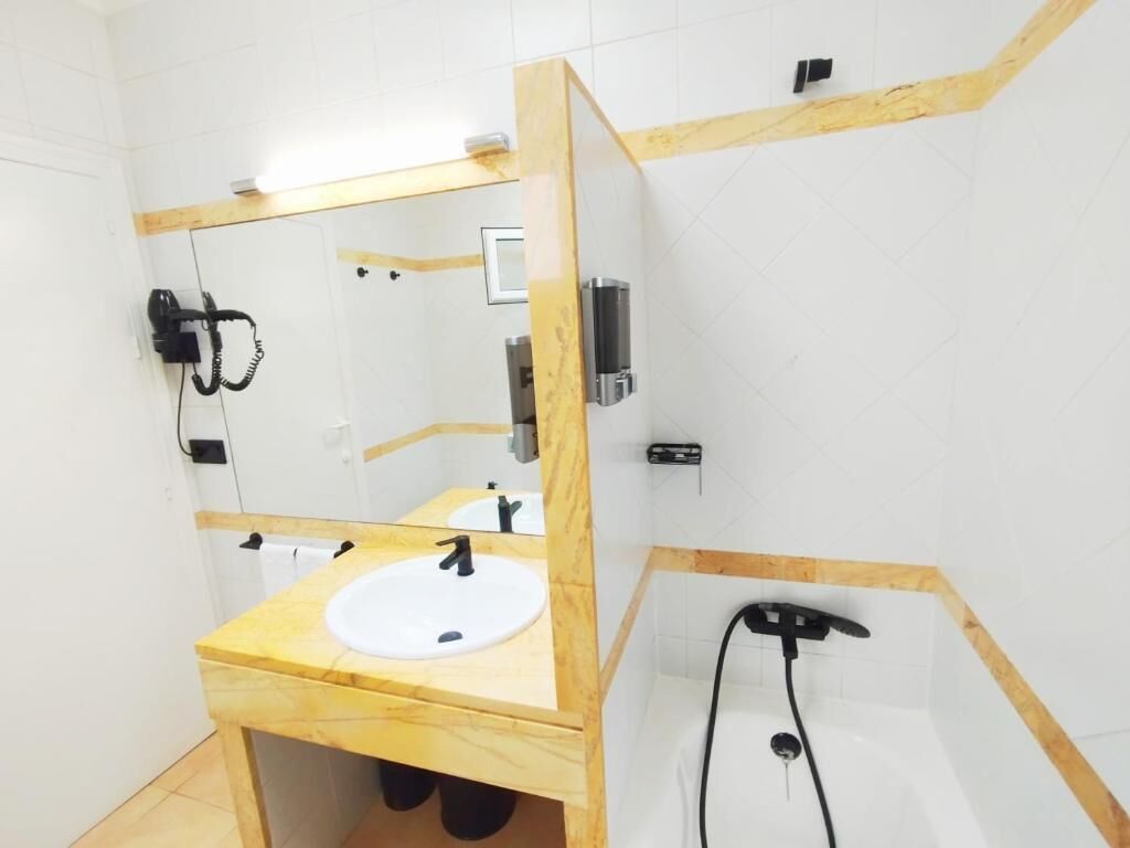 Une salle de bain avec un meuble-lavabo en bois, un évier, un miroir, une douchette à main et un porte-serviettes.