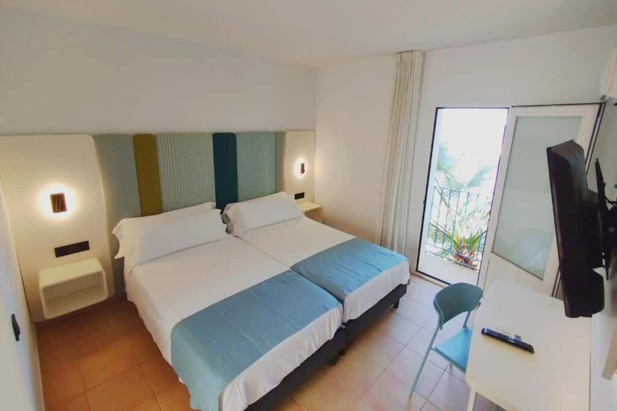 Una habitación de hotel con cama, mesitas de noche, escritorio, silla y televisor.