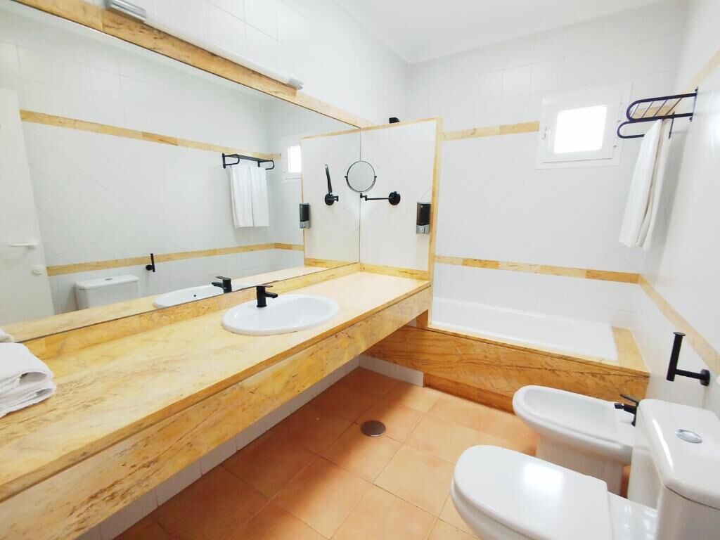 A bathroom with a wooden vanity, two sinks, a bathtub, and a toilet.