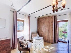 Quarto com guarda-roupa de madeira, mesa redonda com toalha rendada, sofá e lustre.