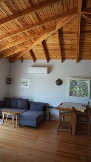 A room with a sloped wooden ceiling, a grey sofa, a small table, and a window with a view of trees.