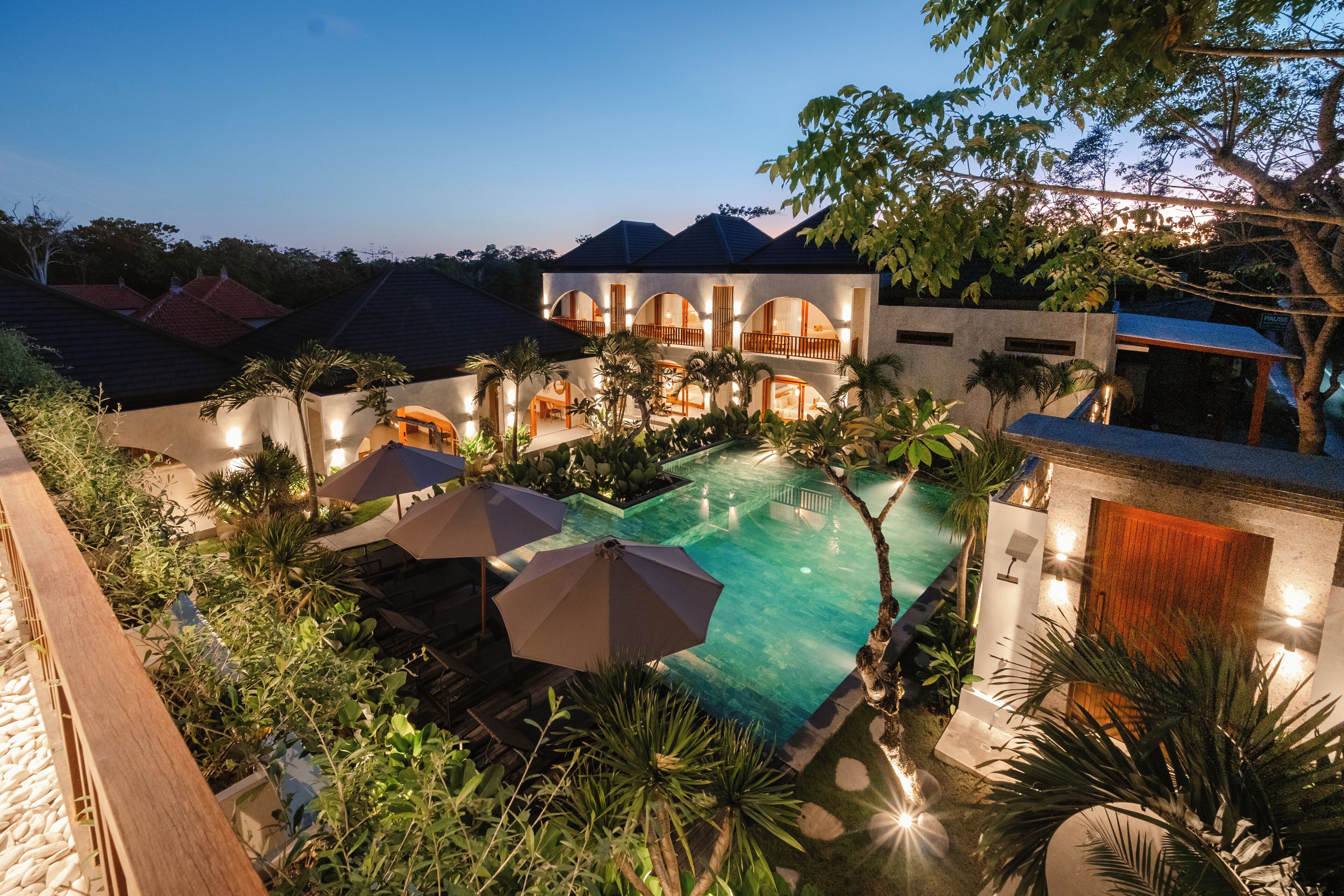 Un resort moderno con piscina, sombrillas exteriores y exuberante vegetación.