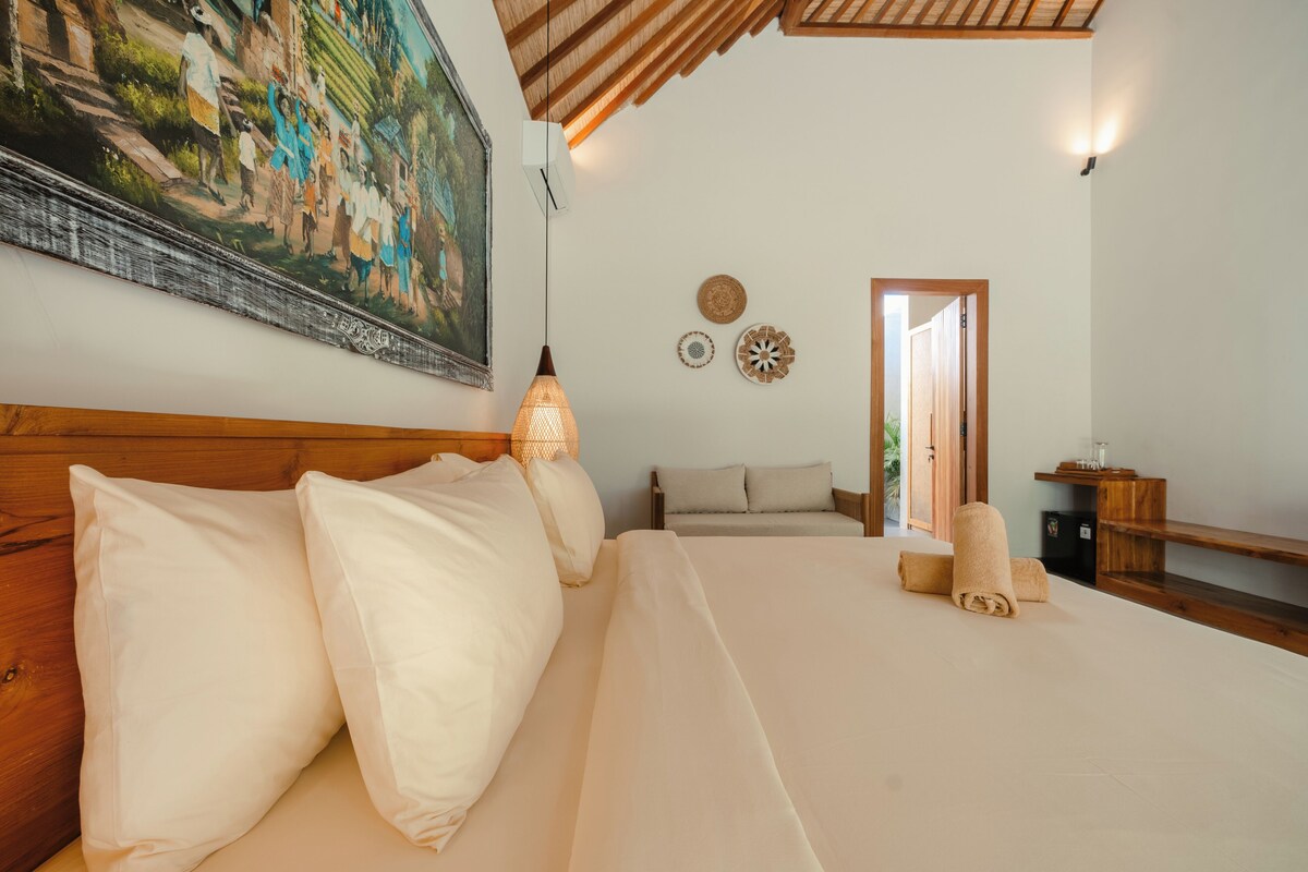 Ein Schlafzimmer mit einem großen Bett, einem Bild an der Wand, einer Nachttischlampe und Blick ins Freie.