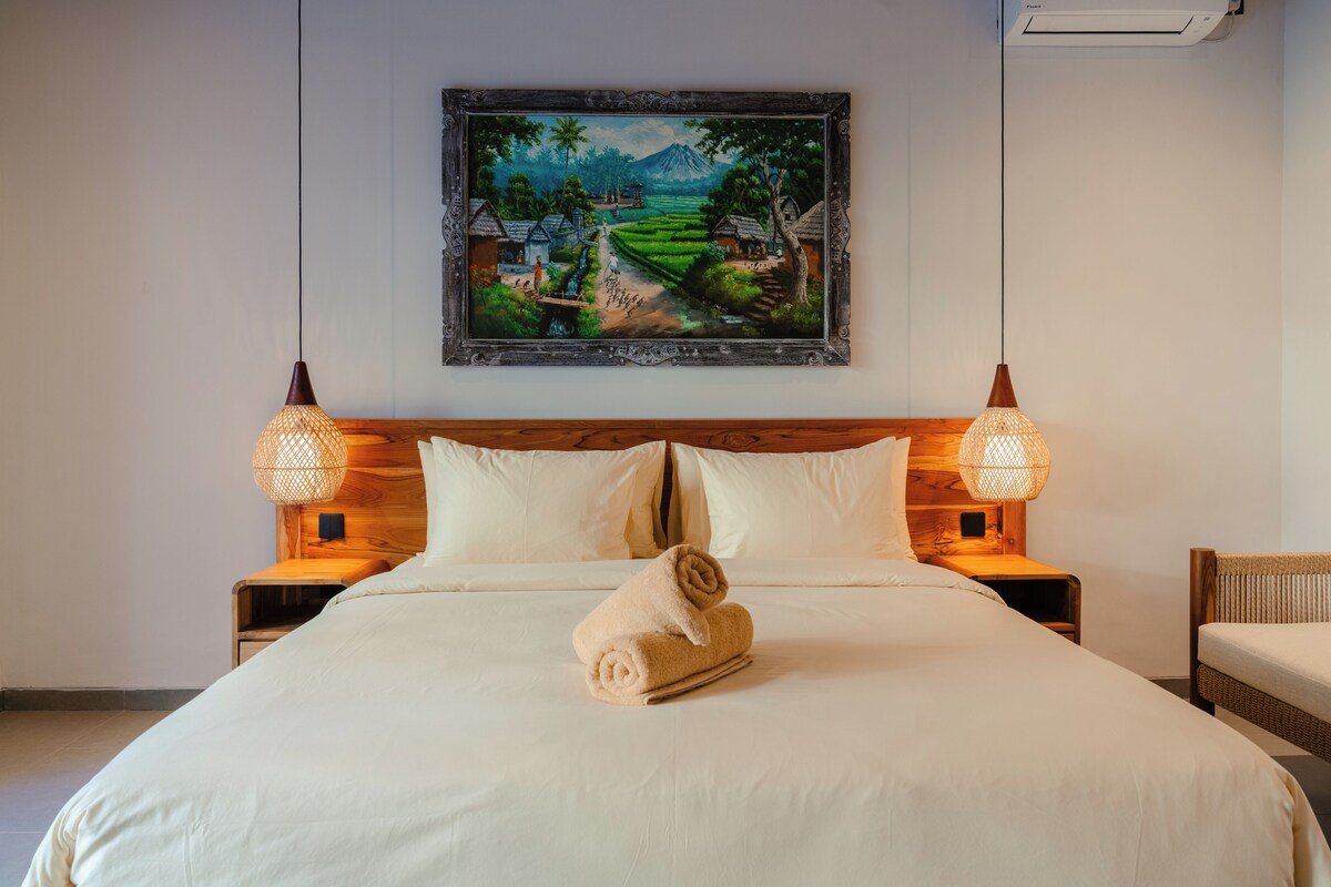 Ein Hotelzimmer mit einem großen Bett, zwei Nachttischlampen, einem Bild an der Wand und einem hölzernen Kopfteil.