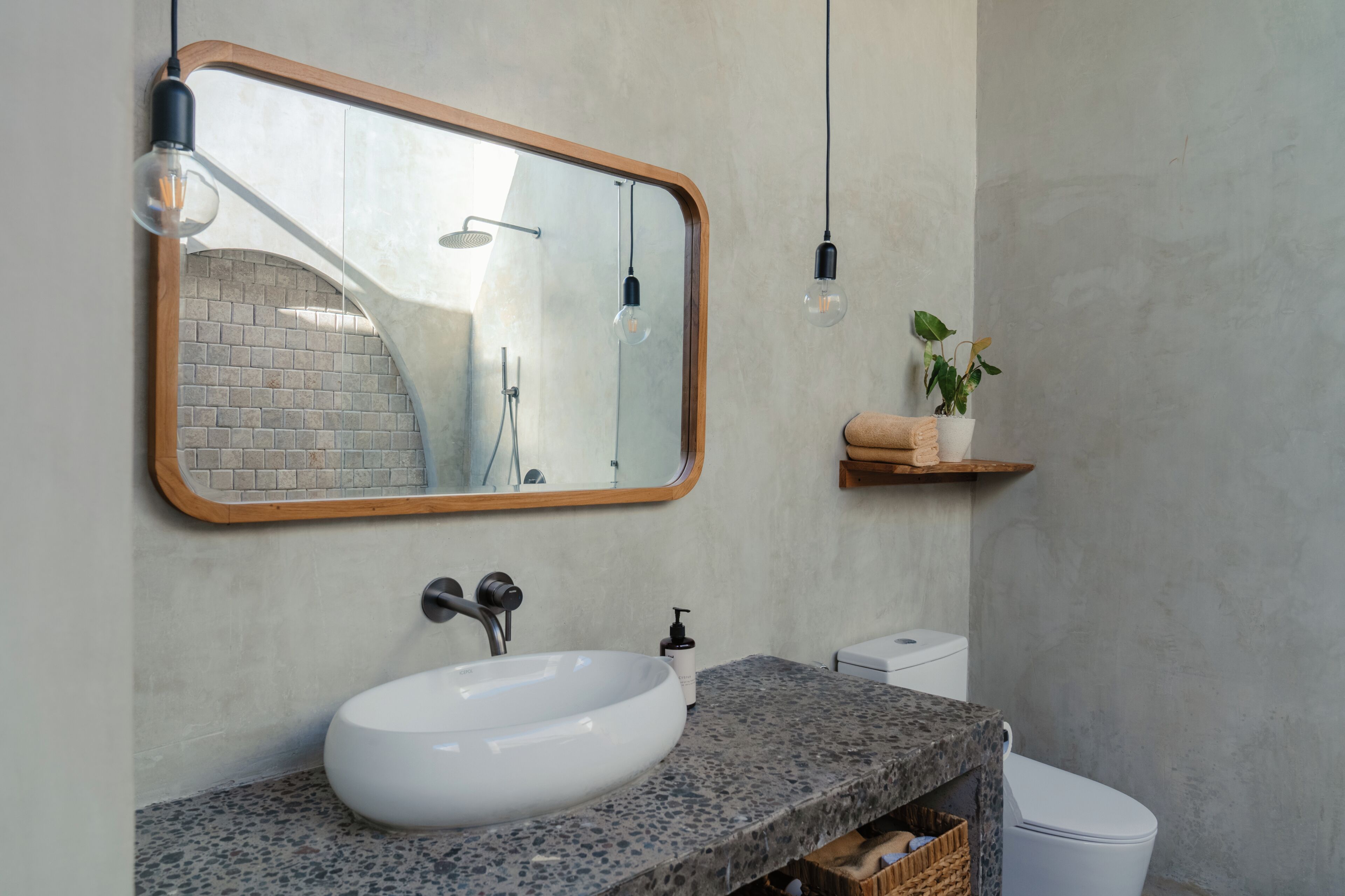A bathroom with a large mirror, a white sink, a towel rack, a potted plant, and a shower.