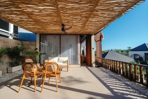 Eine Terrasse im Freien mit Korbmöbeln, einem Deckenventilator und Blick auf die Umgebung.