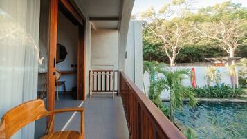 Un balcón con una silla de madera, una mesita y vistas a una piscina y vegetación.