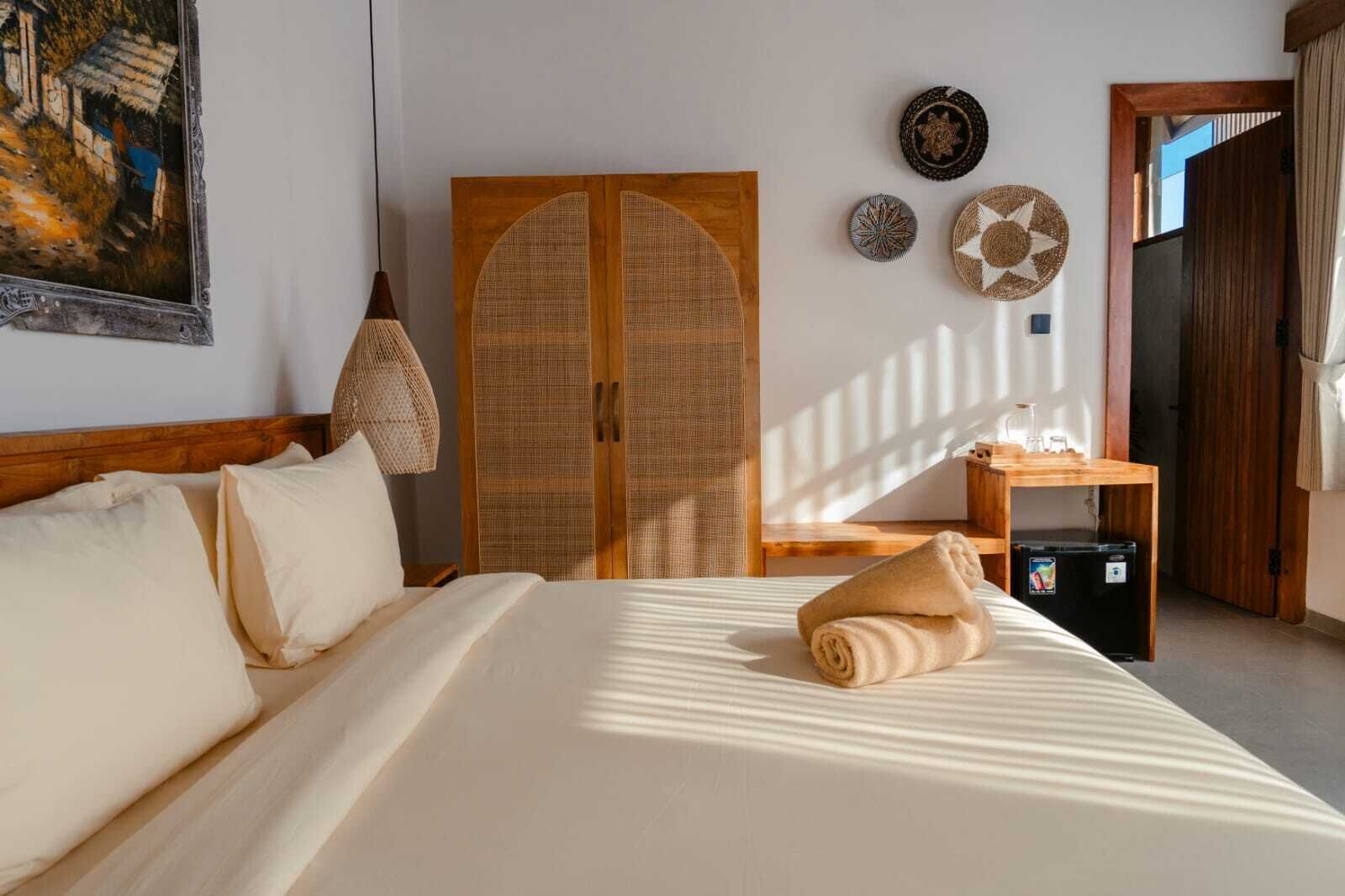 A hotel room with a bed, a wooden wardrobe, a small table with a lamp, and decorative plates on the wall.