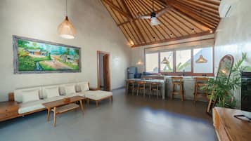 Amplia sala de estar con sofá, mesa de comedor y sillas, cocina con vista y ventilador de techo.