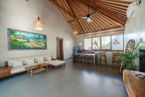 Ein geräumiger Wohnbereich mit Sofa, Esstisch und Stühlen, eine Küche mit Ausblick und einem Deckenventilator.