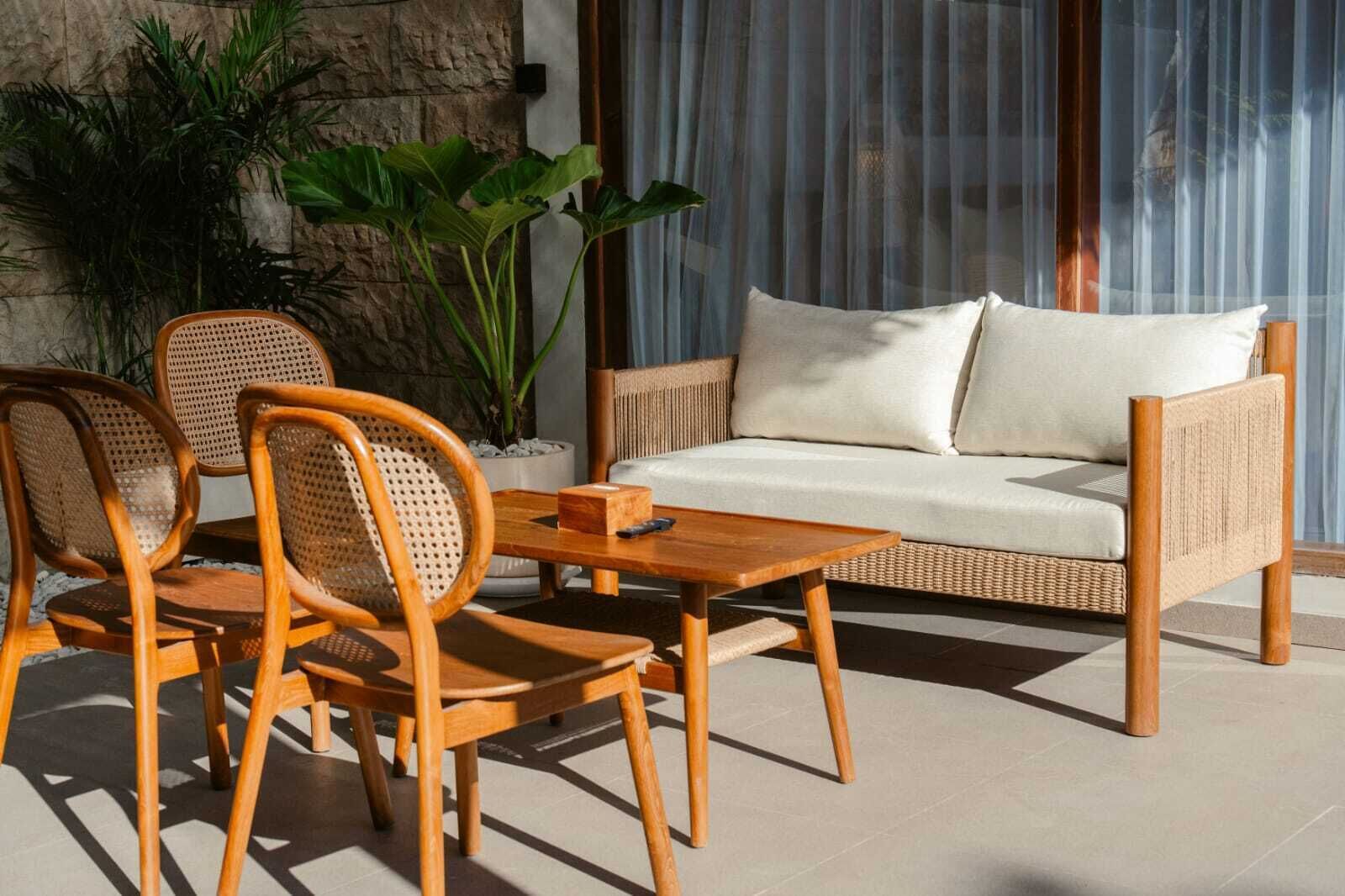 Un sofá de mimbre con cojines, dos sillas de madera con respaldo tejido, una mesita de madera y una planta en maceta.