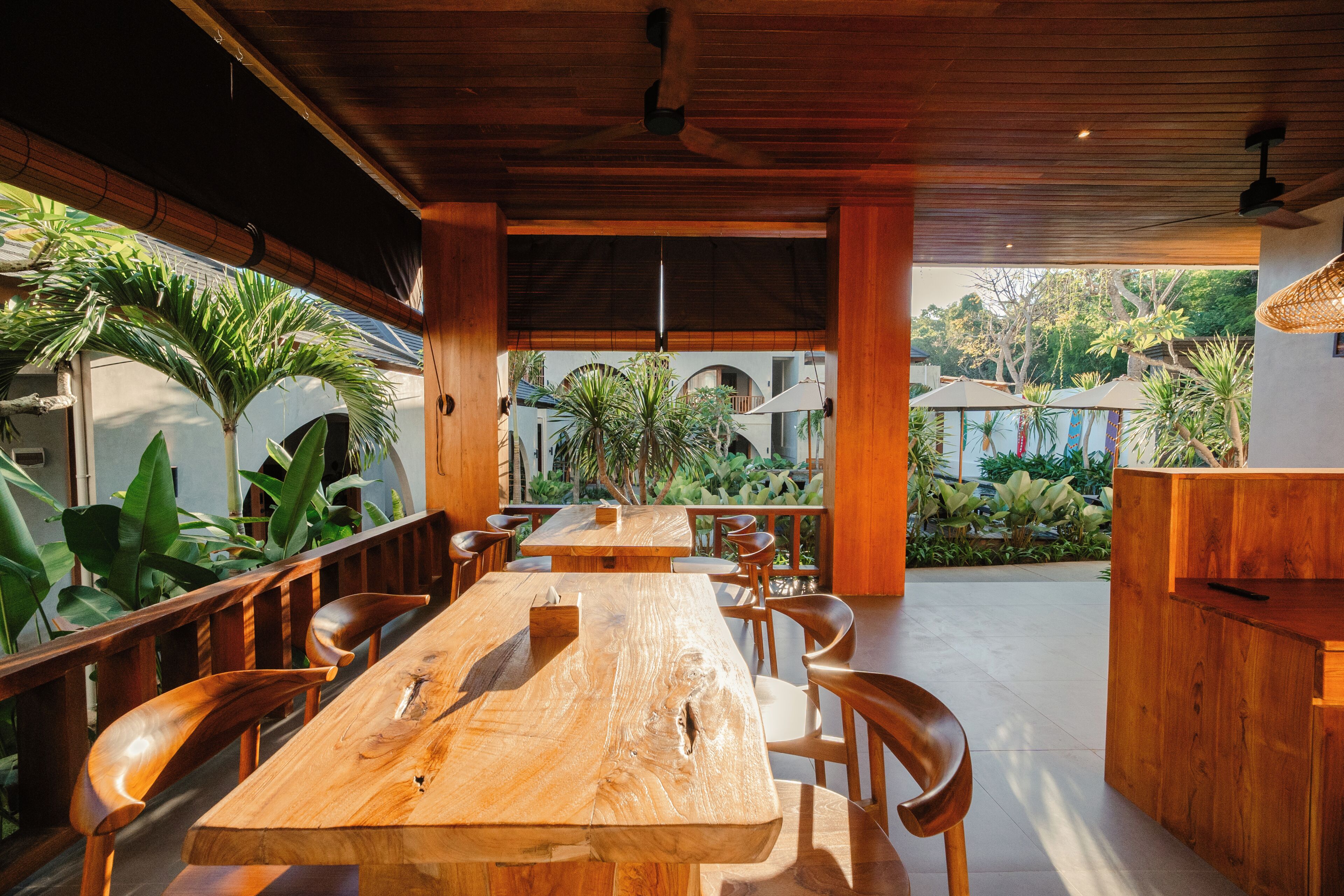 Un comedor interior con mesas y sillas de madera, rodeado de amplios ventanales y plantas.
