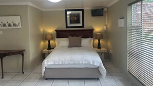 A bedroom with a bed, bedside lamps, a nightstand, a bench, a framed picture, a ceiling light, and a window with blinds. - Six on Green Cottage (Johannesburg)