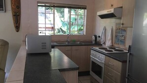 A kitchen with a stove, sink, and window. - Six on Green Cottage (Johannesburg)