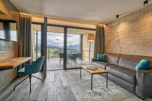 A modern room with a sofa, a table, a chair, and a view of mountains through large windows. - Hotel Avelina (Avelengo)