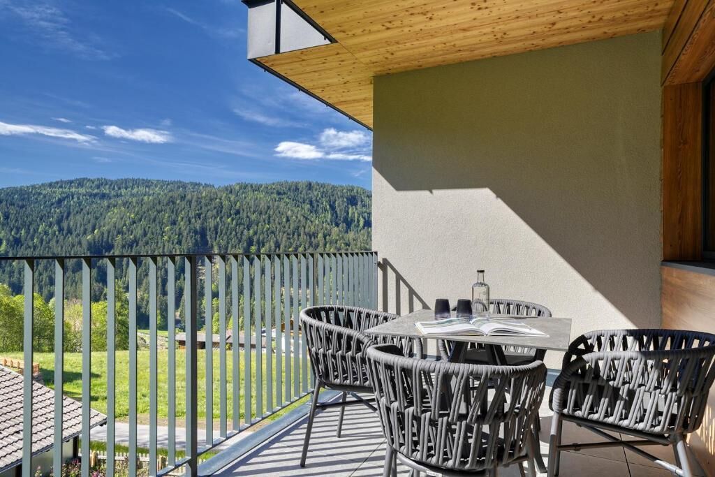 Ein Balkon mit Korbstühlen und einem Tisch, mit Blick auf einen bewaldeten Berg.