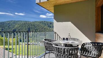 Ein Balkon mit Korbstühlen und einem Tisch, mit Blick auf einen bewaldeten Berg.
