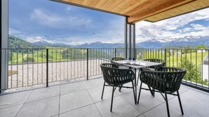 Un balcon avec une table et des chaises, offrant une vue sur les montagnes et un paysage verdoyant.