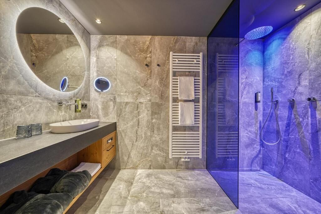 Un baño moderno con un espejo ovalado grande, un lavamanos, un perchero para toallas y una zona de ducha con paredes de vidrio.