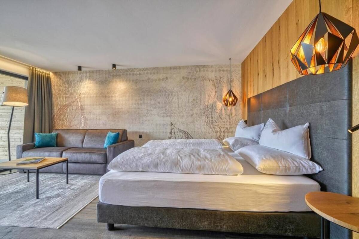 Une chambre moderne avec un grand lit, un canapé, une table basse et un luminaire suspendu au design géométrique original.