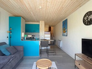 Un intérieur moderne comprenant un canapé, un téléviseur, un coin cuisine et une table à manger.