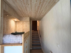 Een smalle gang met een houten trap naar een kamer met een bed en een zithoekje.
