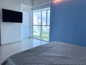 Ein Schlafzimmer mit großem Fenster, einem Bett und einem an der Wand befestigten Flachbildfernseher.
