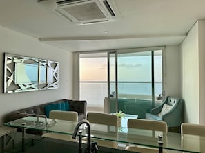 Ein modernes Zimmer mit Glastisch, einer Couch, einem Sessel und Meerblick durch ein großes Fenster.