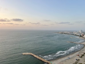 Eine Küstenstadtlandschaft mit Strand, einem Wellenbrecher und hoch aufragenden Gebäuden im Hintergrund.
