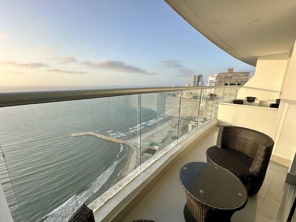 Ein Balkon mit Meer- und Strandblick, Korbmöbel und Glasgeländer.