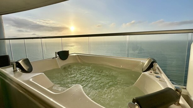 Een bubbelbad met uitzicht op de oceaan en een ondergaande zon.