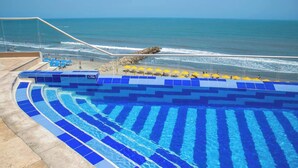 Zwembad met blauwe tegels, een strand en een rotsachtige richel.