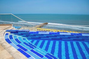 Ein Swimmingpool mit blauen Fliesen, ein Strand und eine Felsformation.