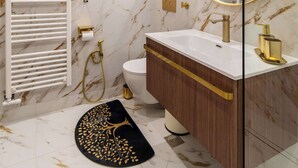 A bathroom with a white sink, gold fixtures, a marble wall, a white towel rack, and a round mirror.