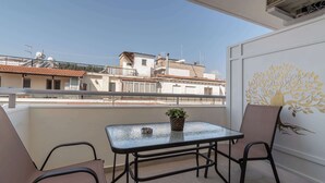 Un balcón con una mesa y sillas, una planta en maceta y un muro decorativo.