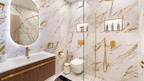 Un baño moderno con pared de mármol, un espejo redondo, un grifo dorado, un inodoro, una ducha y un estante pequeño con artículos de aseo.