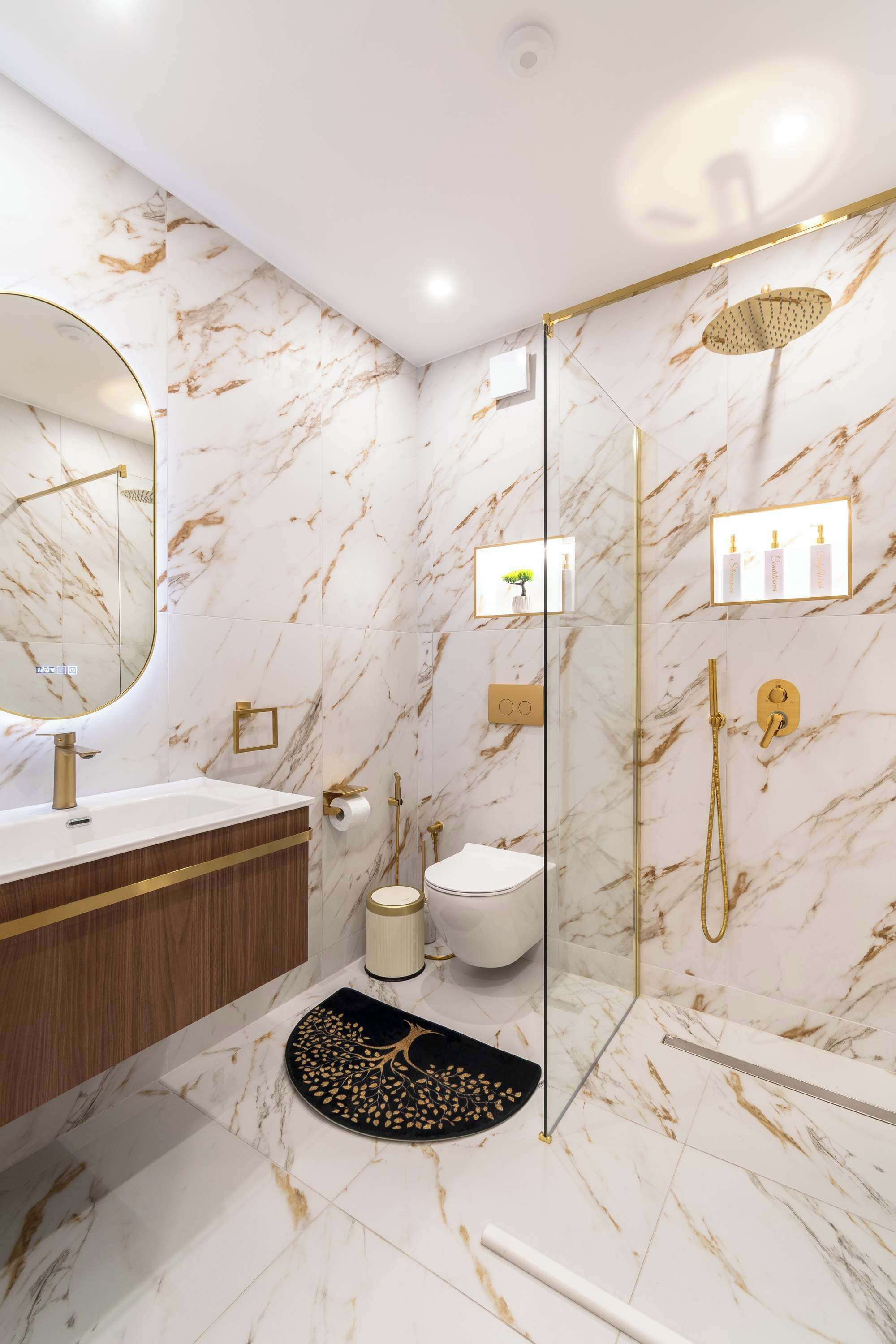 Een moderne badkamer met een marmeren wand, een gouden douche, een witte wastafel en een douchecabine met glazen wanden.