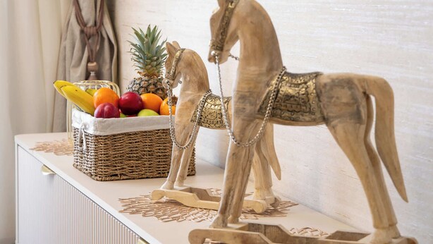 Una sala de estar moderna con un mueble blanco para equipo de entretenimiento, un televisor montado en la pared y figuritas decorativas de caballos.