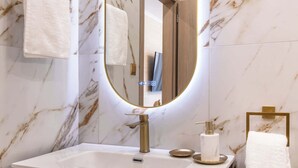 Un baño con pared de mármol, tocador de madera, espejo con marco dorado y toallas blancas.