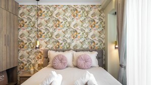 Una cama bien hecha con dos toallas enrolladas, un papel tapiz floral y una lámpara de noche.