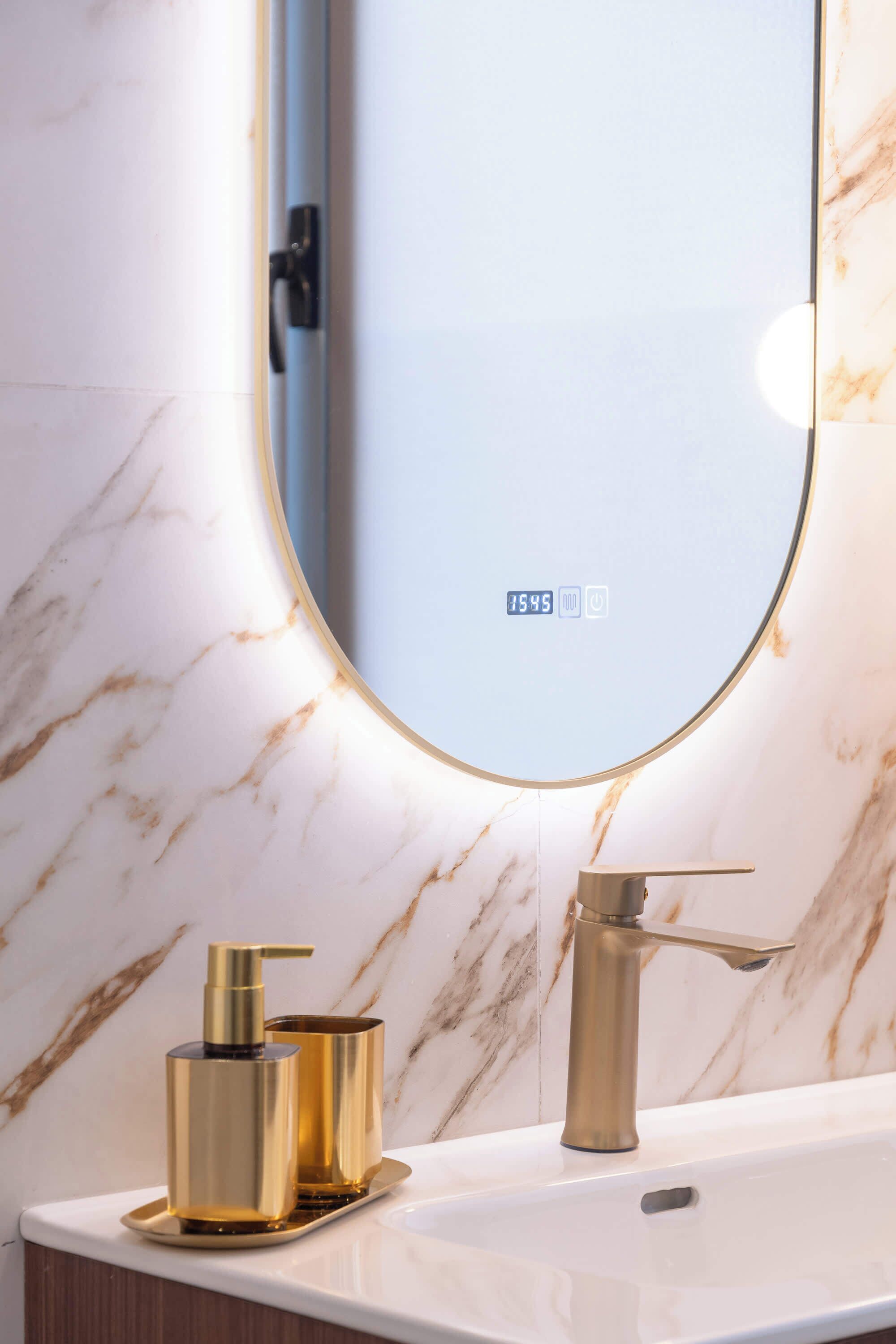 A bathroom with a marble wall, a sink, a gold faucet, and a gold soap dispenser.
