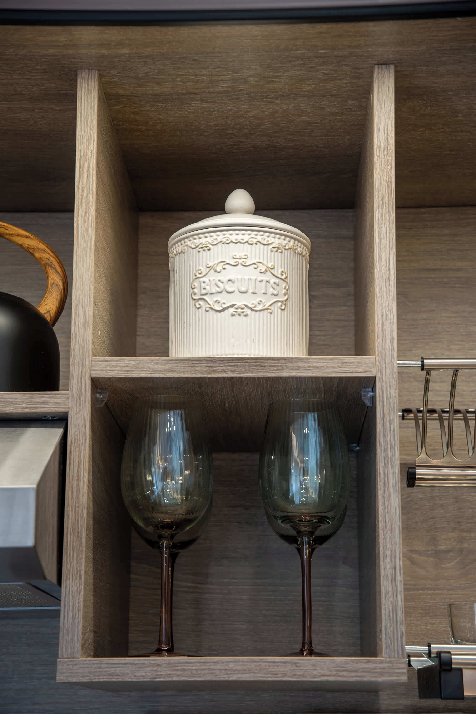 A wooden shelf with a decorative container labeled 'ESCHEETS' and two wine glasses.