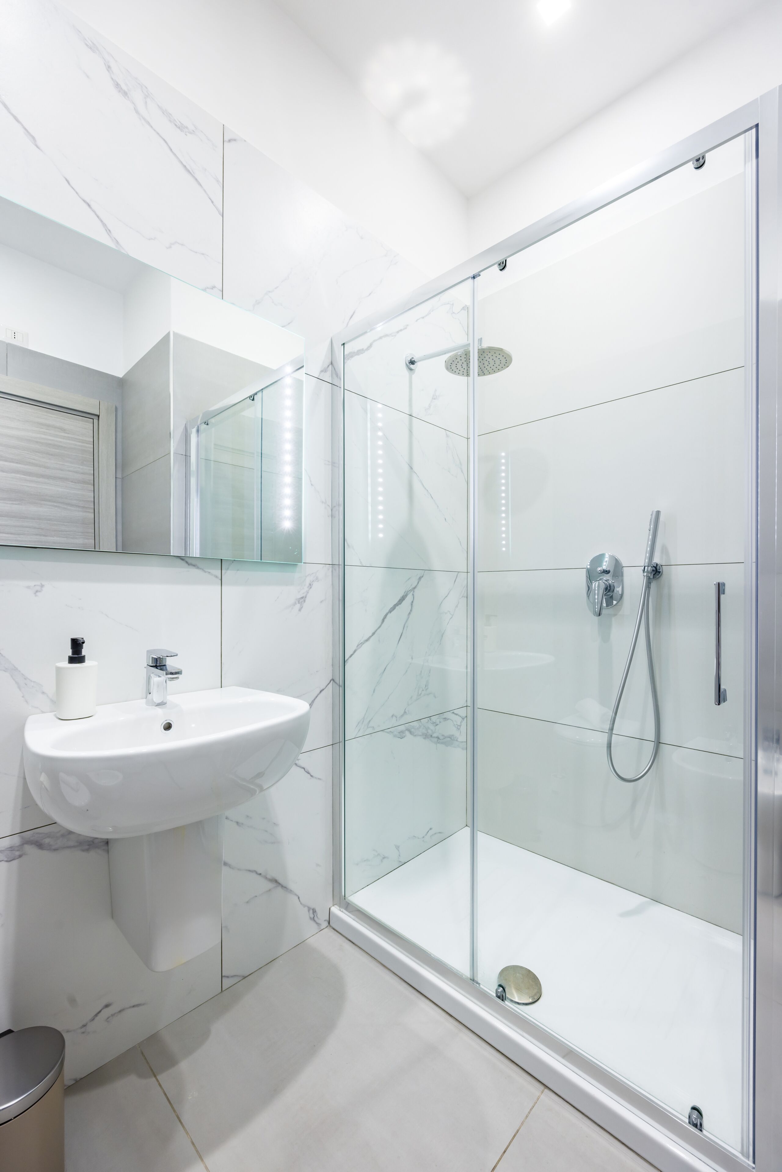 A modern bathroom with a glass-enclosed shower, a white sink, and a marble-tiled wall.