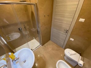 A bathroom with a glass-enclosed shower, a sink, a toilet, and a bidet.