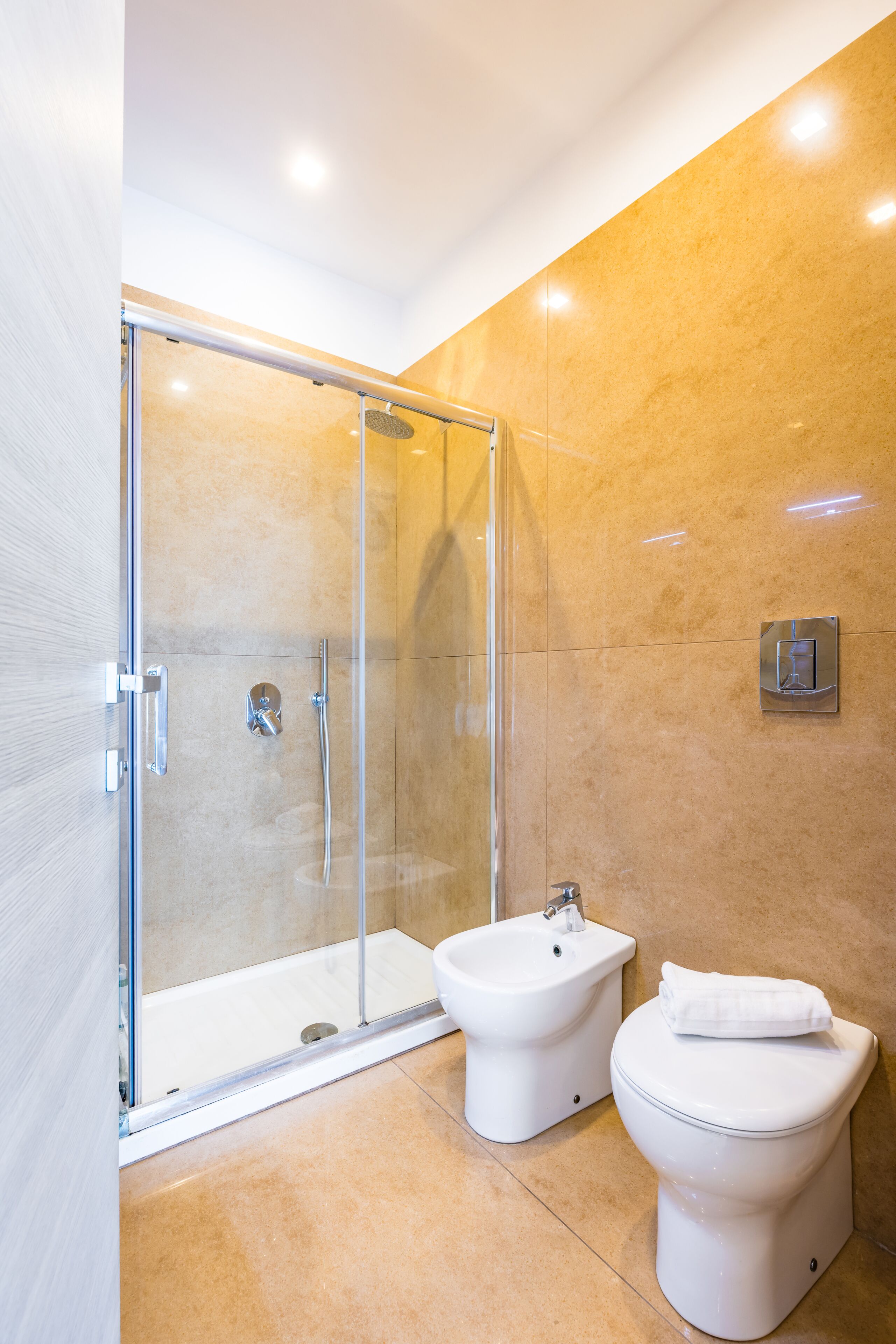 A modern bathroom with a glass-enclosed shower, a bidet, and a toilet.
