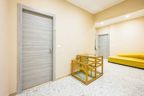 A room with a closed door, a glass-top table, a yellow sofa, and a tiled floor. - MDC Luxury Rooms Naples (Naples)