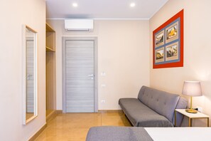 A hotel room with a grey sofa, a small table with a lamp, a wall-mounted air conditioner, and a door leading to a closet. - MDC Luxury Rooms Naples (Naples)